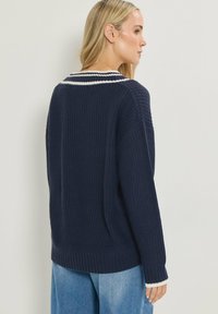 Granatowy sweter dzianinowy z szerokim dekoltem i ściągaczami, z białym paskiem akcentującym przy kołnierzu, w luźnym kroju, widok z tyłu.