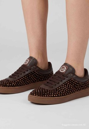 Sneakers marrone scuro con borchie marroni indossate a piedi nudi, con design con lacci e logo "Back 70" sulla linguetta e sul lato della suola.