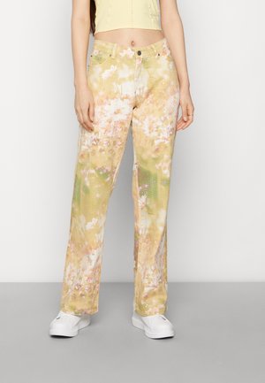 Person wearing yellow floral printed wide-leg pants, white sneakers, and a pale yellow cropped top against a plain white background.
