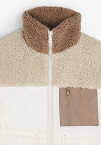 Jachetă din polar cu guler înalt maro, corp crem, fermoar pe față și un buzunar cu fermoar bej. Țesătură texturată cu modele matlasate.