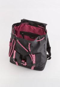 Mochila negra con acentos rosas, que cuenta con un cierre de cuerda, bolsillos exteriores y una textura suave. Forrada con tela rosa.