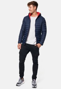 Navy quilted jacket with a red hood, paired with a light gray shirt and black cargo pants. Comfortable fit with zipper closure and pockets.