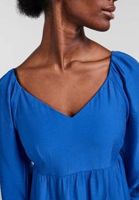 Vestido azul texturizado con un escote en V profundo y mangas recogidas, que muestra una tela suave y fluida sin embellimientos adicionales.
