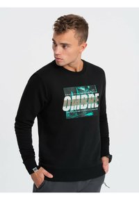 Sudadera negra con un acabado texturizado. Presenta un gráfico destacado que dice "OMBRE" en blanco sobre un diseño abstracto en verde azulado.