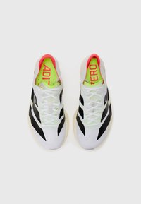 White athletic shoes with black accents, bright green insoles, and a pink collar, featuring lace-up design and textured fabric.