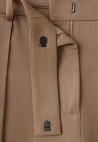Tessuto marrone con una texture diagonale, caratterizzato da dettagli in metallo nero, una cerniera verticale e una tracolla cucita per un fissaggio sicuro.