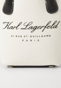 Kreemivärvi keha ja musta nahast detailidega kanvas kott, millel on reljeefne tekst "Karl Lagerfeld 21 RUE ST-GUILLAUME PARIS."
