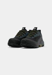Zapatillas de trail running en negro y gris con un diseño texturizado, cordones verdes y suelas rugosas, con un logotipo prominente en la lengüeta.