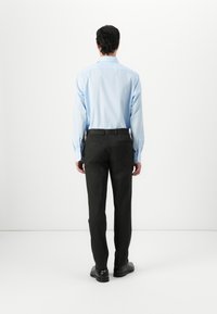 Lichtblauw overhemd met lange mouwen, gecombineerd met donkergrijze op maat gemaakte broek en zwarte schoenen, gezien vanaf de achterkant.