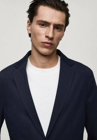 Marineblazer mit Revers, kombiniert mit einem Rundhalsausschnitt-T-Shirt in Weiß. Glattes Material mit maßgeschneiderter Passform, minimalistisches Design und klare Linien.