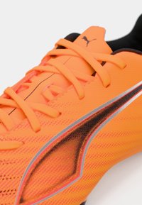 Scarpino da calcio Puma di un brillante arancione con una tomaia texturizzata, accenti neri e lacci piatti. Caratterizzato da un design elegante e dettagli riflettenti.