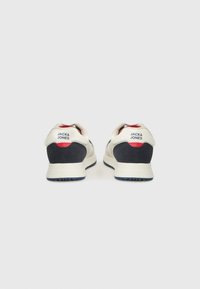 White and navy athletic shoes featuring a textured design, padded collar, and red accents, with branding on the heel. Rubber outsole.