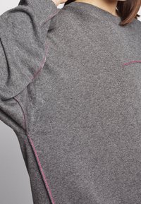Gray sweater featuring a round neck, contrasting pink stitching along the seams, and a soft texture, showcasing a smooth, minimalist design.