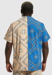 Kortermet skjorte med brune og blå halvdeler, med paisley-mønstre, blomsterdesign og kontrastfarger, laget av lett stoff.