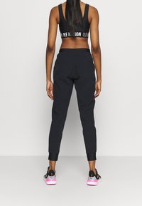 Svarta atletiska joggers med avsmalnande ben och enhetliga anklar, i kombination med en svart sportbh med vit loggan, bärs med svarta och rosa sneakers.