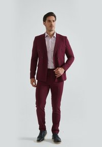 Costume bordeaux à double boutonnage avec pantalon ajusté, associé à une chemise légère à motifs et des chaussures en cuir noires. Tissu lisse avec coupe ajustée.