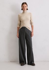 Beige Rollkragenpullover und graue weit geschnittene Wollhose. Die Hose hat eine hohe Taille, klare Linien und ein minimalistisches Design. Braune Schuhe runden das Outfit ab.