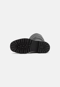 Suela de bota de goma negra con patrones de pisada profundos, que presenta un borde elevado y una superficie plana para tracción y estabilidad.