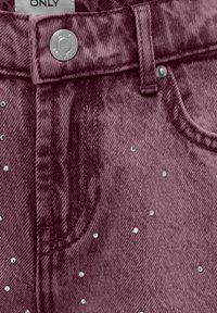 Vynuose spalvos džinsai su tekstūruotu paviršiumi, sidabro spalvos mygtukų užtrauktuku ir išsibarsčiusiomis blizgančiomis akmenimis.