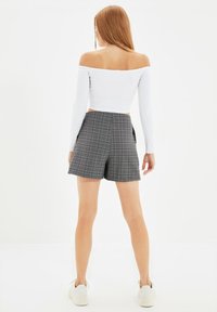 Weißes, schulterfreies Crop-Top kombiniert mit grauen, karierten Shorts mit hoher Taille. Die Shorts zeichnen sich durch einen taillierten Schnitt und Gesäßtaschen aus.