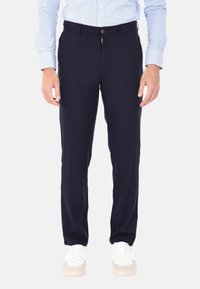 Pantaloni blu navy con una vestibilità regolare, dotati di zip e chiusura a bottone. Realizzati in un tessuto morbido, abbinati a sneaker bianche.