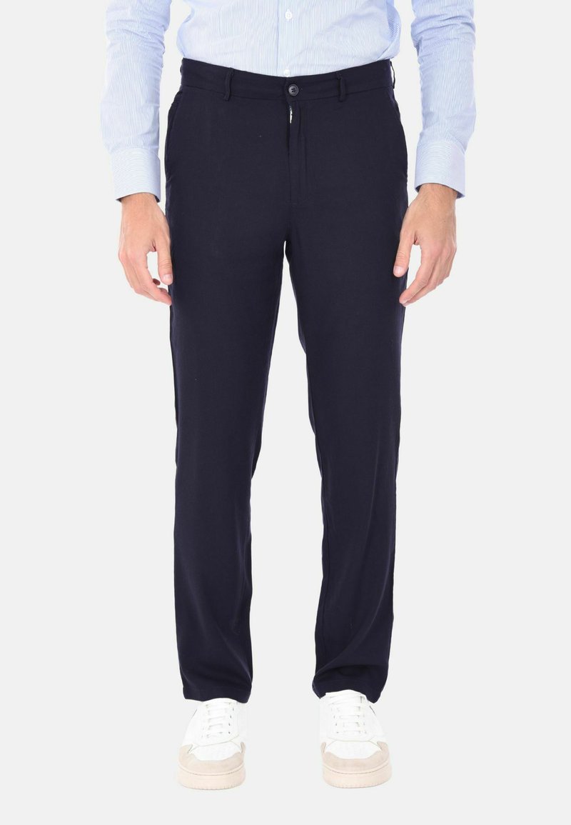 Pantaloni blu navy con una vestibilità regolare, dotati di zip e chiusura a bottone. Realizzati in un tessuto morbido, abbinati a sneaker bianche.