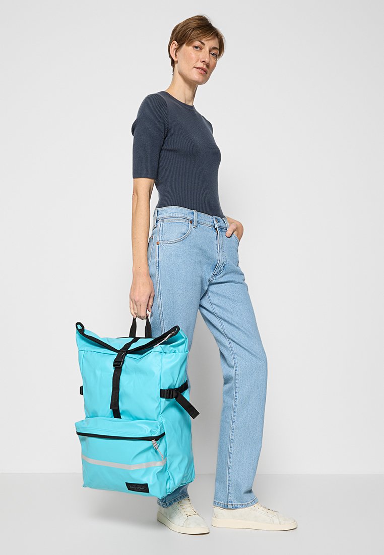 Türkisfarbene Rucksack mit verstellbaren Trägern, Rolltop-Design, Fronttasche mit Reißverschluss, schwarzen Akzenten und einer glatten, wasserdichten Textur.