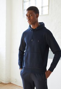 Felpa blu navy realizzata in tessuto morbido, con tasca frontale, cappuccio con cordino e piccolo logo sul petto. Progettata con polsini a costine.