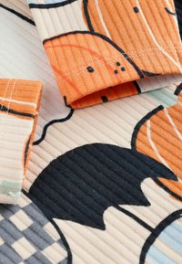 Puuvillakangas, jossa on uritettu rakenne, oransseja kurpitsoja, musta lepako ja geometrisiä kuvioita harmaassa ja kerma väreissä.