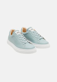 Sneakers in pelle azzurro chiaro con suole in gomma bianca, punta rotonda, cuciture tonali e un'etichetta sul retro. Logo visibile sulla linguetta.