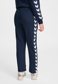 Marineblauwe joggingsbroek met een wit zigzagpatroon aan de zijkant, voorzien van een elastische tailleband en boorden, gecombineerd met lichte sneakers.