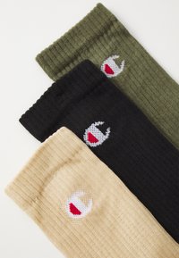 Drei Paar Socken in olivgrün, schwarz und beige. Jede Socke hat eine gerippte Textur und ein Logo mit roten und weißen Akzenten.