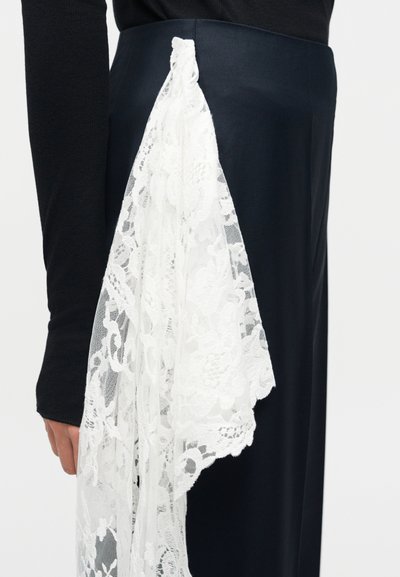 Μαύρη φούστα με λεπτομέρεια λευκού φλοράλ δαντέλας που κρέμεται από τη μέση, σε συνδυασμό με μαύρο τοπ μακρυμάνικο σε ένα άτομο.