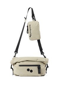 Beige Umhängetasche mit Rollverschluss, Frontreißverschlussfach, zwei schwarzen Punkten auf der Vorderseite und einem abnehmbaren kleineren Beutel mit verstellbarem schwarzen Tragegurt.