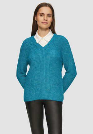 Turquoise gebreide trui met een V-hals, voorzien van een gestructureerd patroon en ribbels. Gecombineerd met een witte blouse met kraag en donkere broek.