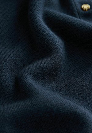 Navy blue knit fabric featuring a textured surface, with gentle folds and a gold button accent visible, conveying softness and warmth.