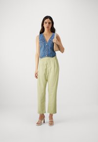 Denimvest med v-hals, frontknapper og lommer; lysegrønne høytlivsbukser; hvite hælhæler; beige håndveske.