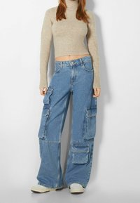 Beige ribbad polokrage-tröja kombinerad med vida blå denim cargobyxor som har fyra stora fickor och en lös passform.