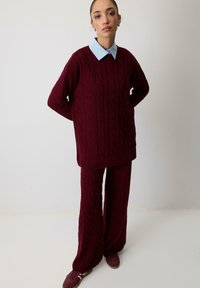 Tumepruun kootud sviiter ja sobivad laiad püksid, kantud kerge sinise kraepliisiga särgi peale, millel on soonikused mansetid ja äär.