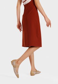 Ballerine beige Mary Jane con pannelli in rete, punta arrotondata e dettaglio a fibbia, abbinate a un vestito rosso ruggine a lunghezza ginocchio.