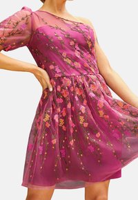 Fuksianvärinen mekko, jossa on läpikuultava yksivartinen hiha, pinkillä ja oranssilla kirjailtu kukkakuvio, vyötäröltä kerrostettu ja liehuva helma.