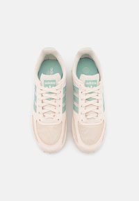 Beige sneakers with mesh and fabric materials, featuring light blue stripes and logo on the tongue. Rounded toe and lace-up design.