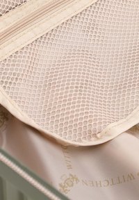 Taschina con zip in rete beige con motivo esagonale, all'interno di un compartimento in tessuto chiaro con una stampa del logo discreta.