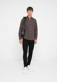 Brun skjorte med knapper og frontlomme, parret med svarte slim-fit bukser og hvite joggesko. Skjorten har et teksturert stoff og krage.