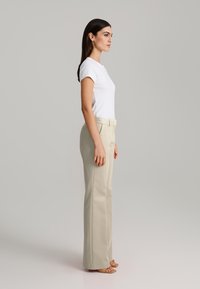 White fitted t-shirt paired with light beige high-waisted trousers, featuring a smooth texture and a flared silhouette.