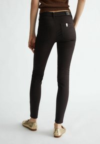 Zwarte skinny jeans met een hoge tailleband, vijf zakken en een klein metalen label op de achterkant. De stof lijkt soepel en aansluitend.