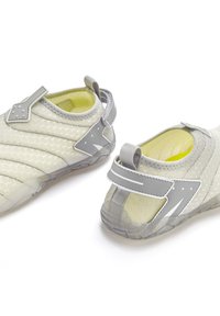 Helle graue Sportschuhe mit einer strukturierten Oberfläche, verstellbarem Riemen und gelber Innenausstattung. Merkmale einer flexiblen Sohle mit einem gemusterten Design.