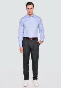 Jasnoniebieska koszula z długim rękawem, szare spodnie w wzory, brązowy pasek i białe sneakersy. Koszula ma kołnierzyk z guzikami i gładką fakturę.