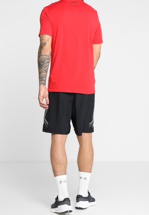 Mann trägt ein rotes Kurzarmshirt, schwarze Shorts mit reflektierenden Details, weiße Markensocken und schwarze Laufschuhe, steht mit dem Rücken zum Betrachter.
