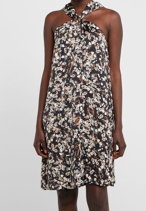 Vestido negro sin mangas con estampado floral blanco y marrón, con cuello halter retorcido, llevado por una persona de pie.